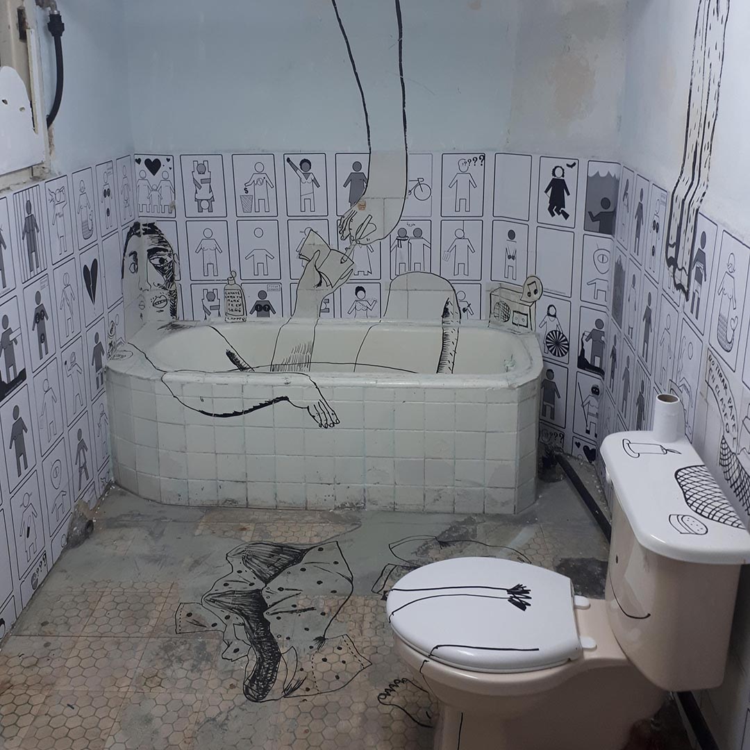 Photo of an old bathroom Coco has illustrated over in black market. There is a cartoon person lying in the bathtub.